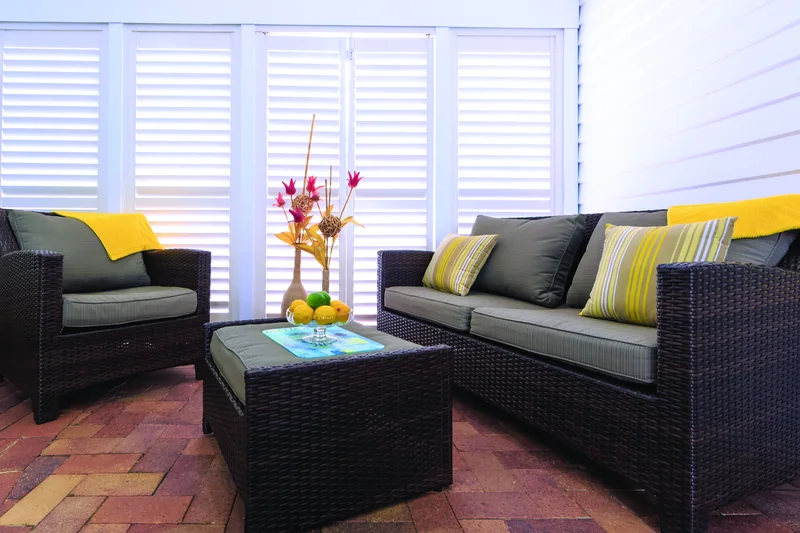White plantation shutters enclosing a covered patio with rattan lounge seating