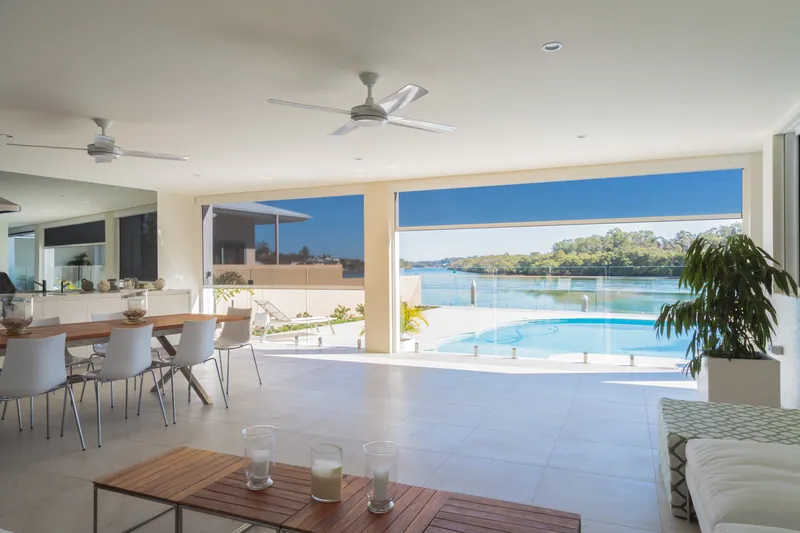 Alfresco dining area beside a pool with ZipScreens raised, opening to the water view